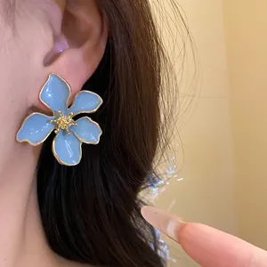 Detailed view of light blue flower stud earrings with golden edges on model's ear