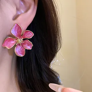 Detail of a pink enamel flower earring with gold edges on an Asian model's ear.