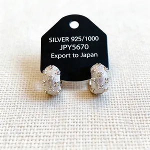 Detailed view of textured silver hoop earrings with clear zircon stones on a black card