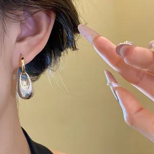 Close-up of elegant textured silver waterdrop pendant hoop earring worn on the ear