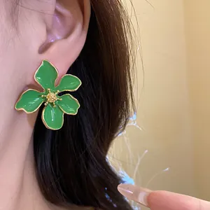 Close-up of large green enamel flower stud earring worn on ear, fresh resort style