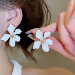 Detail of elegant white drip oil flower stud earrings with gold trim on model.