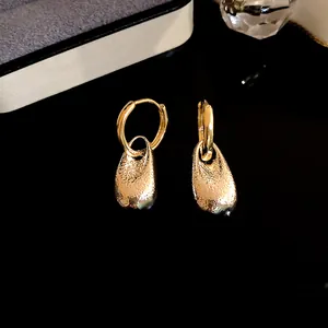 Detailed view of gold-colored textured water drop earrings on a dark reflective surface