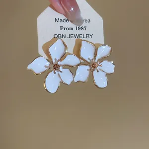 Close-up of luxury white enamel flower stud earrings with gold plating on a jewelry card