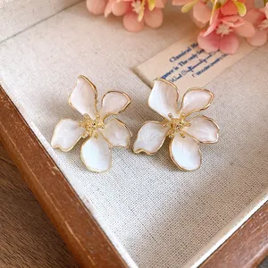 Close-up of white enamel flower stud earrings with golden edges on a wooden tray