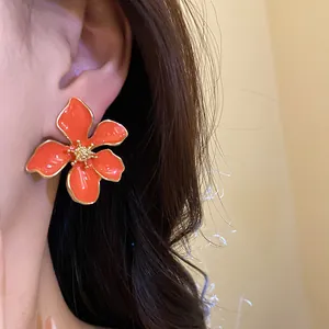 Detailed close-up showing a bright orange enamel flower stud earring worn on an earlobe