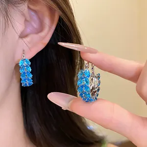 Detailed view of elegant blue zircon wheat ear hoop earrings worn and held by hand