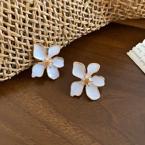 Macro detail view of elegant white enamel flower stud earrings with gold plating on wood