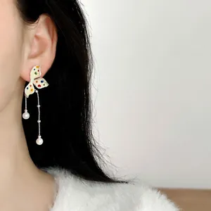 Close-up of colorful polka dot flower earrings with elegant pearl tassels on model.