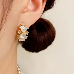 Elegante witte bloemen oorbellen met gouden details en kristallen op een modeloor