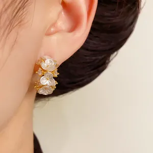 Detailopname van Franse elegante gouden oorbellen met witte schelpenbloemen en zirkonia