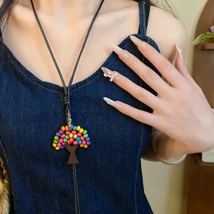 Gros plan d'un collier avec pendentif arbre en perles de bois colorées sur cordon noir.