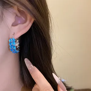 Macro detail of blue zircon wheat ear hoop earrings elegantly worn on an Asian model's ear.