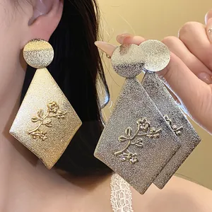 Close-up of metallic rhombus earrings with engraved flower pattern in gold and silver