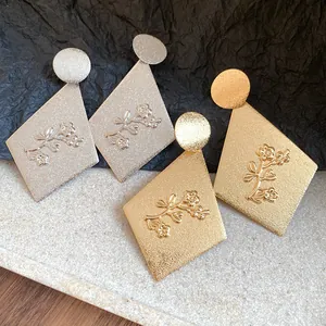 Macro detail of textured metal rhomboid earrings with delicate embossed floral pattern.