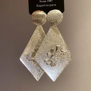 Close-up detail of silver diamond-shaped drop earrings with floral textured pattern