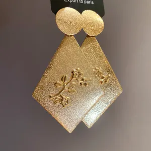 Macro detail of gold rhombus earrings with intricate metallic flower relief.