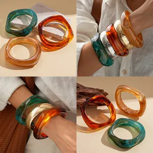 Detailed view of layered retro irregular wide resin bangles in amber and emerald green tones