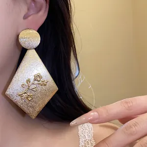 Close-up of a large gold diamond earring with elegant floral texture worn by a model