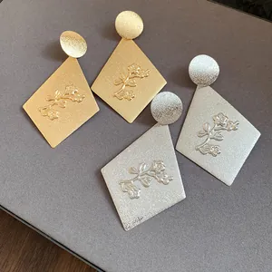 Close-up of gold and silver metallic rhombus earrings with embossed floral details