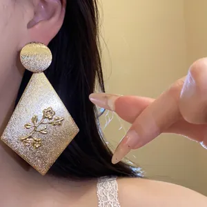 Macro view of golden diamond-shaped drop earrings with embossed flower detail