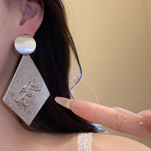 Close-up of elegant silver rhombus drop earrings with floral relief on model's ear