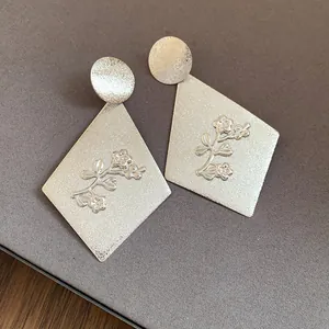 Close-up detail of matte silver rhombus earrings with an embossed floral branch design