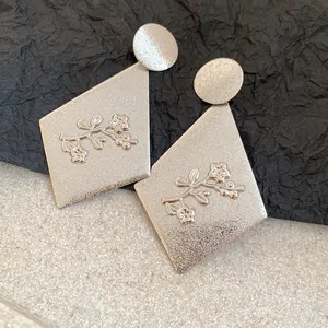 Close-up of silver metal diamond drop earrings with elegant floral relief pattern detail.