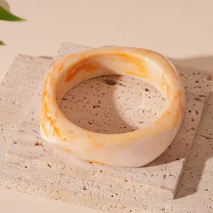 Close-up of irregular wide resin bangle with warm orange Maillard marbled pattern