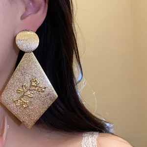 Detailed close-up view of elegant gold rhombus drop earrings with floral embossed pattern