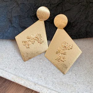 Macro detail of elegant gold metallic diamond earrings with engraved floral branch patterns