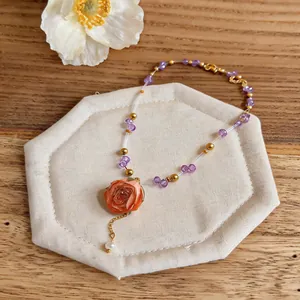 Detail view of a beaded necklace with an orange preserved rose and purple crystals.