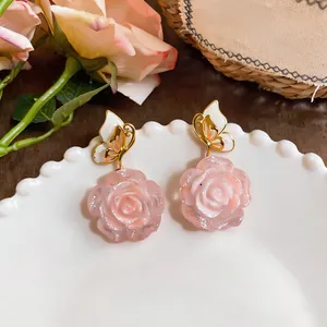 Detailed macro shot of elegant pink resin rose earrings with gold butterfly accents