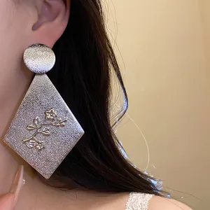 Close-up detail of silver geometric rhombus earrings featuring embossed floral design