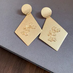 Close-up detail of elegant gold rhombus dangle earrings with embossed floral design.