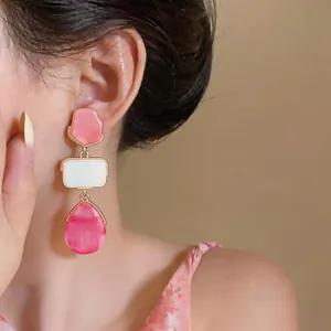 Primo piano di orecchini a goccia geometrici in resina rosa e bianca con bordo dorato.