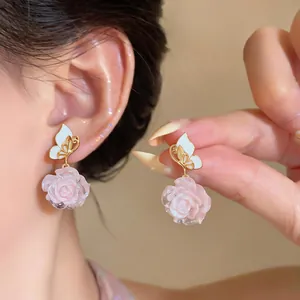 Close-up detail of elegant butterfly and pink rose dangle earrings worn on a female ear