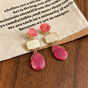Dettaglio di orecchini a goccia in resina con strati geometrici in rosa e crema