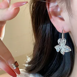 Close-up detail showing a hollow butterfly earring with blue zircons on a model's ear.
