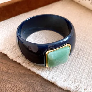 Close-up of navy blue acrylic bangle with a square green marbled stone and gold frame.