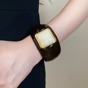 Detail of a chunky dark brown acrylic bangle with a square marble-effect center inlay