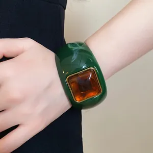 Close-up detail of a bold green acrylic geometric bangle with amber square stone