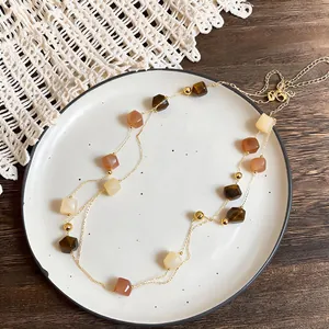 Dettaglio della collana boho a doppio strato con pietre cubiche terrose su catena dorata.