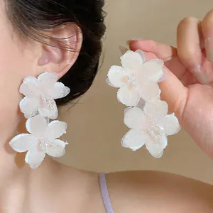 Detail view of elegant oversized chiffon flower earrings with glass beads on a model.