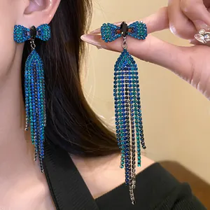 Close-up detail of luxury silver needle bowknot tassel earrings with blue and green rhinestones