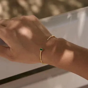 Detail showing a gold open cuff bracelet with a green emerald-cut zircon on a wrist