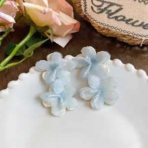 Macro view of light blue chiffon flower stud earrings featuring elegant glass bead centers