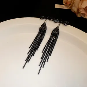 Macro view of elegant black rhinestone bowknot tassel earrings on a white ceramic plate