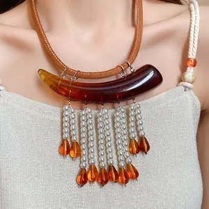 Dettaglio di una collana stile Maillard con acrilico ambrato e nappe di perle bianche.