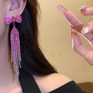 Close-up of sparkling pink rhinestone bow tassel drop earrings worn by a female model
